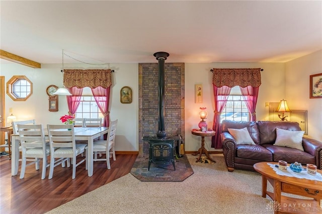 living room featuring plenty of natural light, beam ceiling, wood-type flooring, and a wood stove