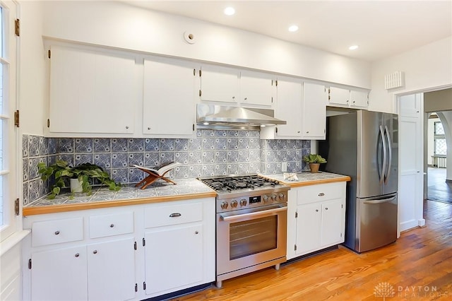 kitchen featuring white cabinetry, backsplash, stainless steel appliances, and light wood-type flooring