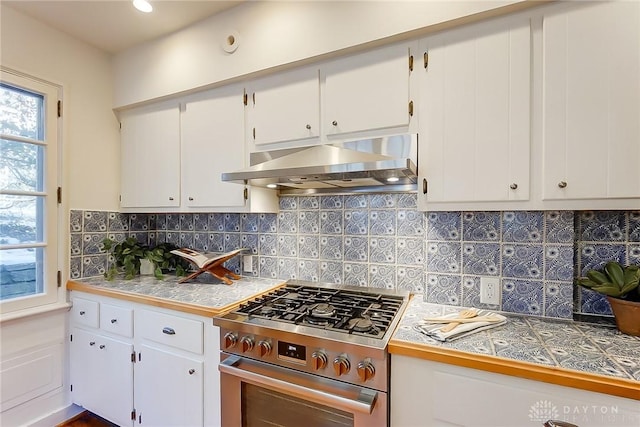 kitchen with white cabinetry, backsplash, tile countertops, and stainless steel gas range oven