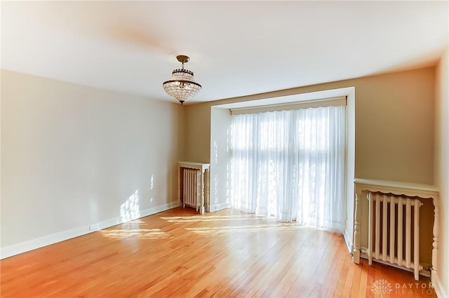 empty room with radiator, a notable chandelier, and wood-type flooring