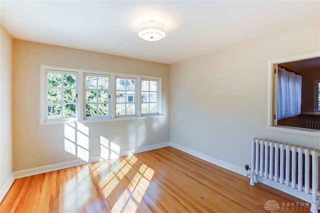 unfurnished room featuring hardwood / wood-style flooring, radiator heating unit, and a wealth of natural light