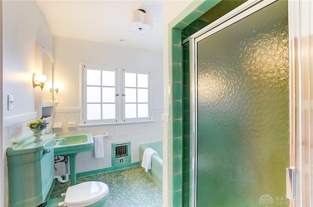 bathroom featuring heating unit, a shower with shower door, tile walls, and toilet