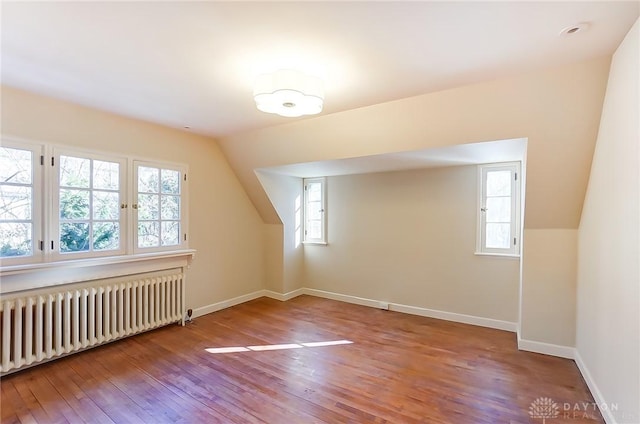 additional living space featuring a wealth of natural light, vaulted ceiling, wood-type flooring, and radiator heating unit