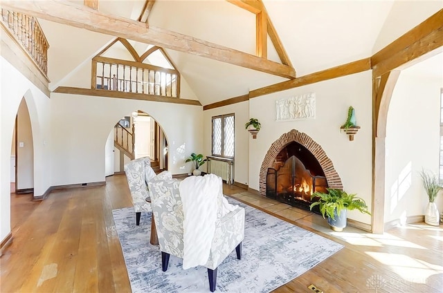 sitting room featuring beamed ceiling, high vaulted ceiling, hardwood / wood-style floors, and a brick fireplace