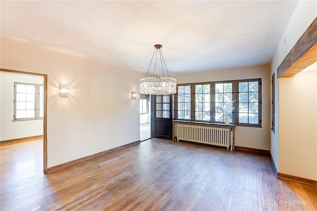 empty room with a notable chandelier, radiator heating unit, hardwood / wood-style floors, and a wealth of natural light