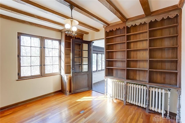 empty room with an inviting chandelier, radiator, beam ceiling, and light wood-type flooring