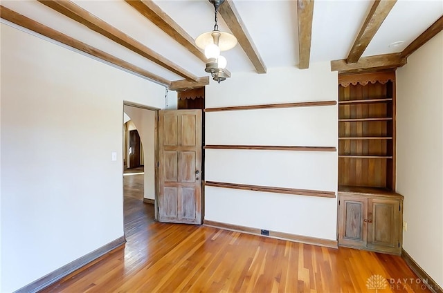 empty room featuring beamed ceiling and light hardwood / wood-style floors