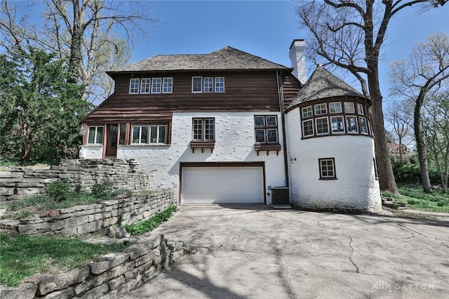1515 Woodstock Dr, Oakwood, OH 45419 - view of front of house with a chimney, concrete driveway, an attached garage, cooling unit, and brick siding