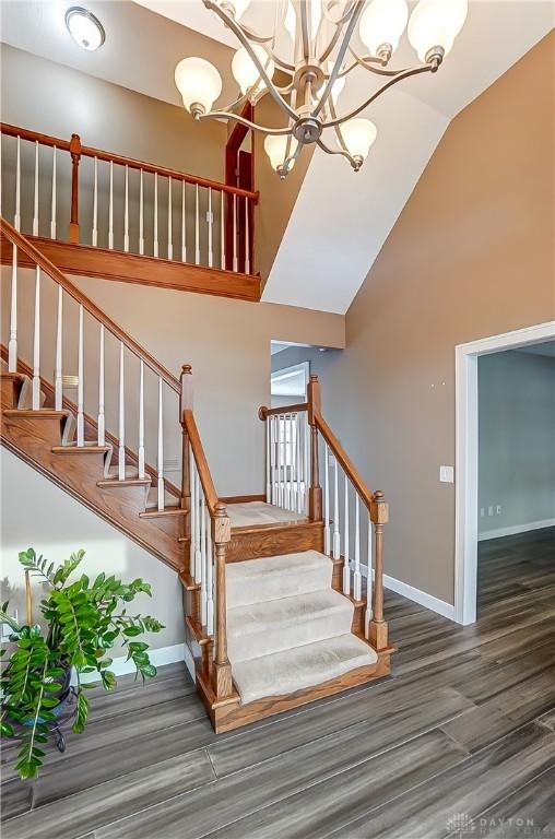 stairs featuring hardwood / wood-style flooring, a notable chandelier, and high vaulted ceiling