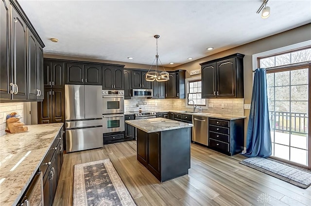 kitchen featuring a kitchen island, decorative light fixtures, sink, stainless steel appliances, and light stone countertops