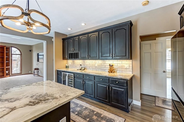 kitchen with dark wood-type flooring, wine cooler, light stone counters, a chandelier, and decorative backsplash