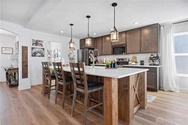 kitchen with a center island with sink, stainless steel appliances, dark brown cabinetry, a kitchen bar, and light wood-type flooring