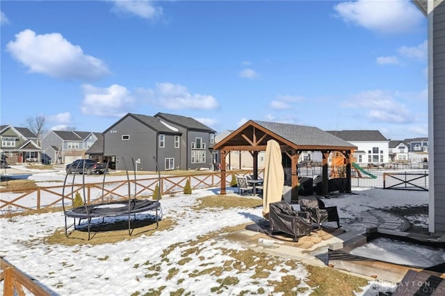 snowy yard with a trampoline, a residential view, fence, and a playground