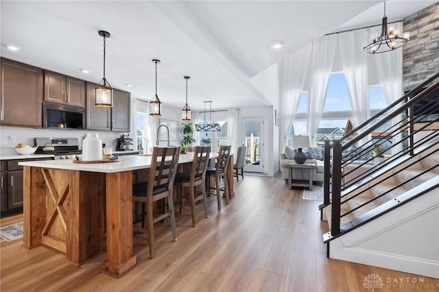 kitchen featuring pendant lighting, a kitchen island with sink, stainless steel appliances, dark brown cabinetry, and light hardwood / wood-style floors