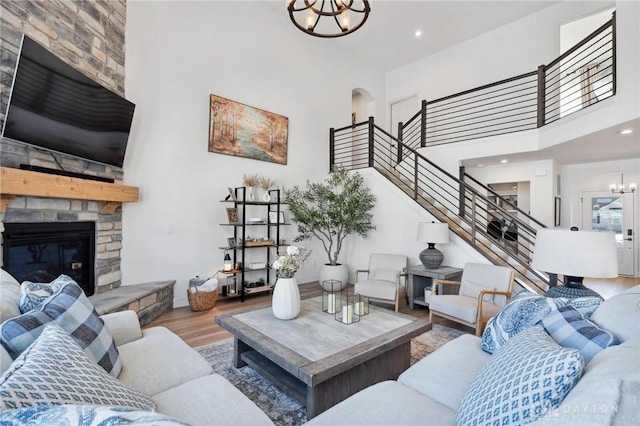 living room with a towering ceiling, wood-type flooring, a fireplace, and a notable chandelier