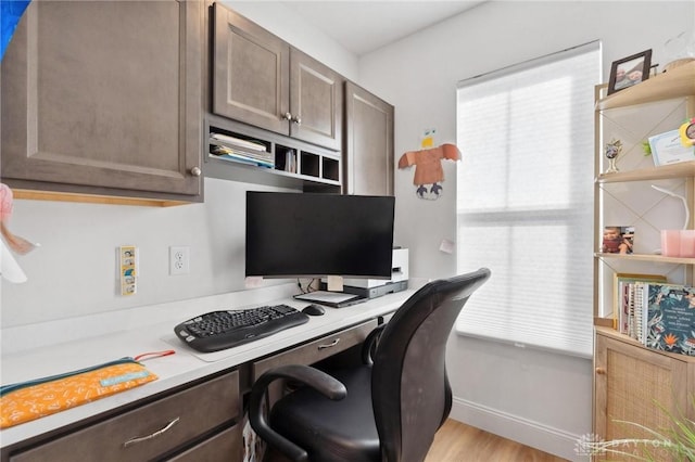 office area featuring light wood-style flooring, baseboards, and built in desk