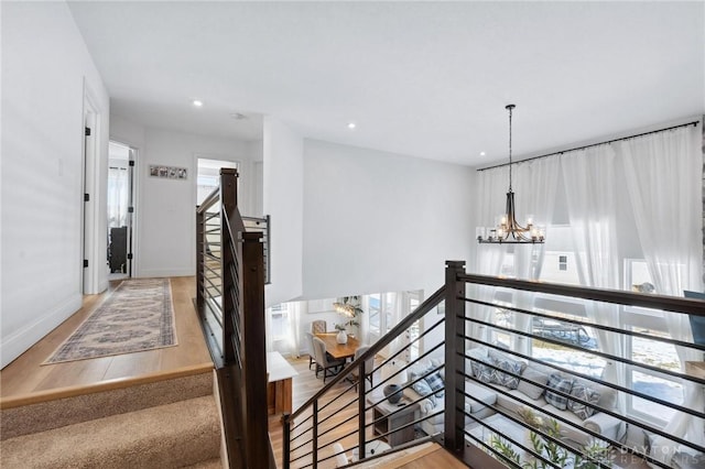 hallway with baseboards, a healthy amount of sunlight, an upstairs landing, and an inviting chandelier