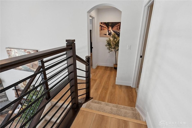 hall featuring arched walkways, baseboards, and wood finished floors