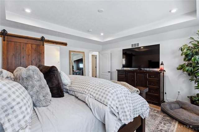 bedroom featuring a barn door, visible vents, and a tray ceiling