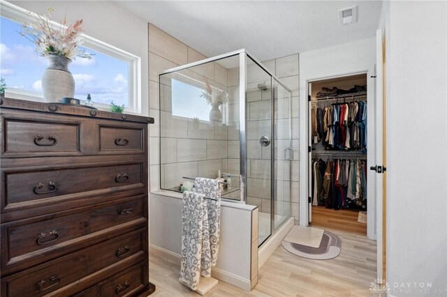 full bathroom with a stall shower, a spacious closet, visible vents, and wood finished floors