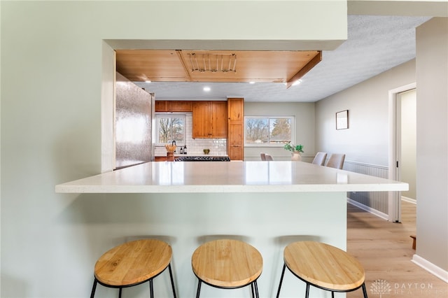 kitchen with decorative backsplash, light hardwood / wood-style flooring, a kitchen breakfast bar, and kitchen peninsula