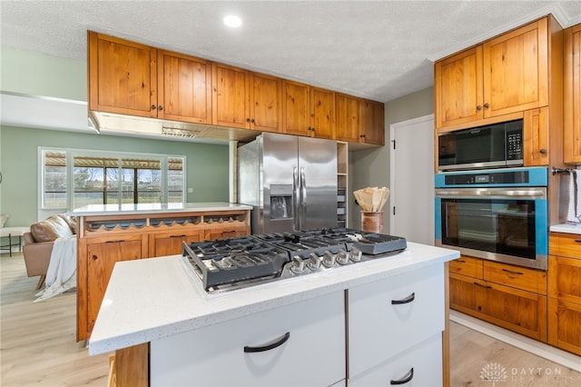 kitchen with a kitchen island, light hardwood / wood-style floors, a textured ceiling, and appliances with stainless steel finishes