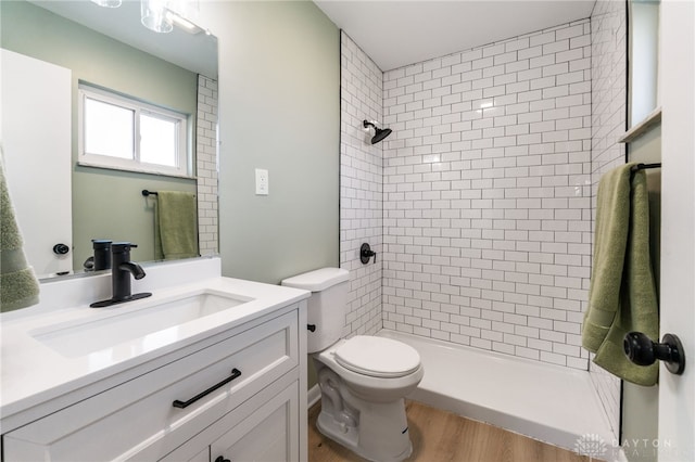 bathroom featuring vanity, wood-type flooring, toilet, and tiled shower