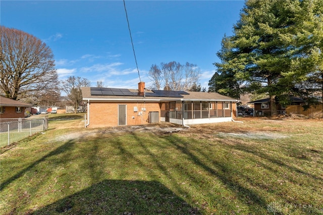 rear view of property featuring a lawn, a sunroom, and solar panels