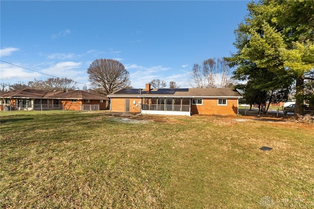 back of property with a yard, a sunroom, and solar panels