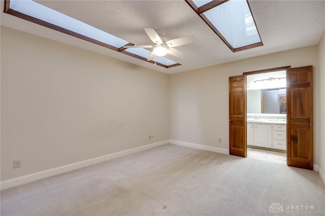 unfurnished bedroom featuring light carpet, connected bathroom, a skylight, and a textured ceiling