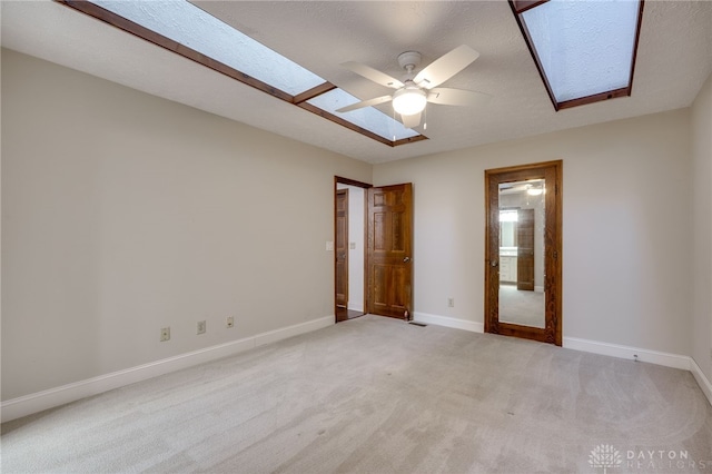 unfurnished bedroom with light carpet, a textured ceiling, ceiling fan, and a skylight