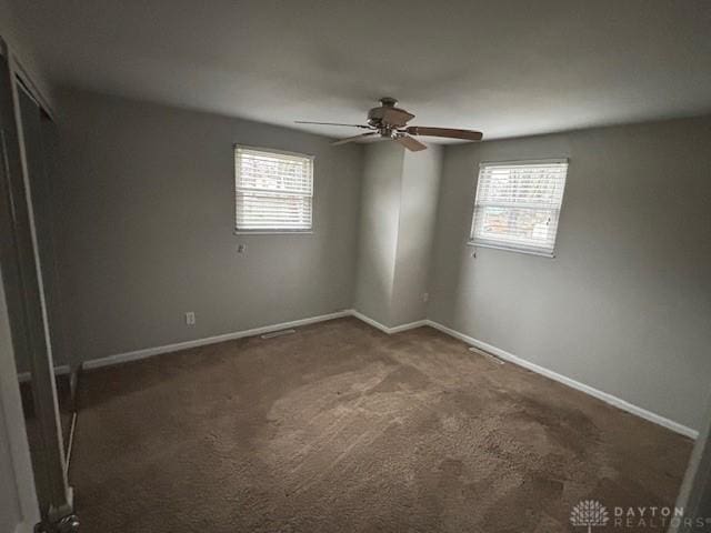 empty room with dark colored carpet, a healthy amount of sunlight, and ceiling fan