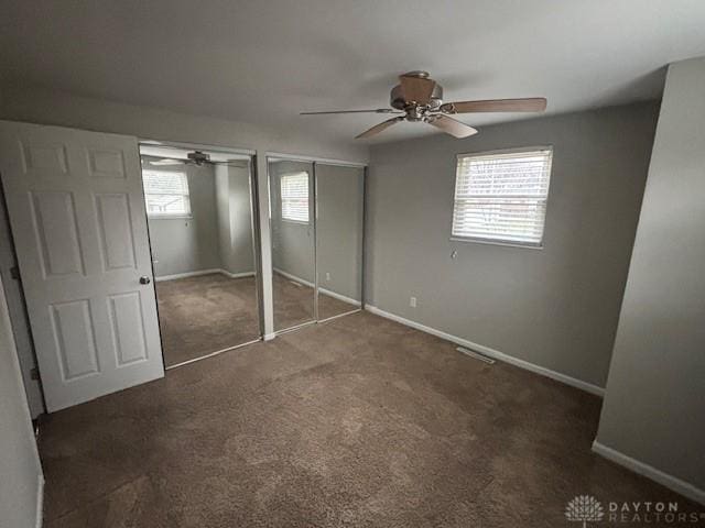 unfurnished bedroom featuring multiple closets, ceiling fan, and dark carpet