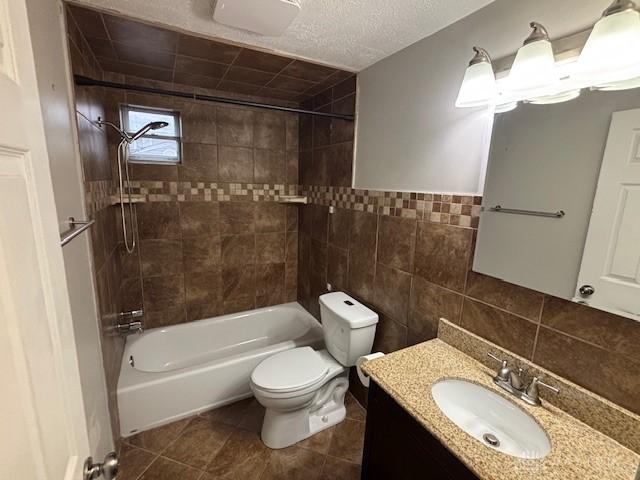 full bathroom featuring tile patterned floors, toilet, tiled shower / bath, tile walls, and vanity