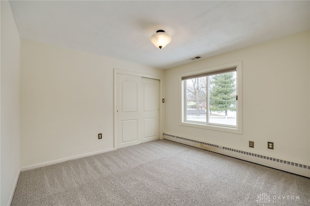 carpeted empty room featuring a baseboard heating unit