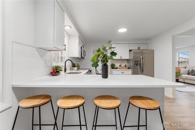 kitchen featuring sink, white cabinetry, backsplash, stainless steel appliances, and kitchen peninsula