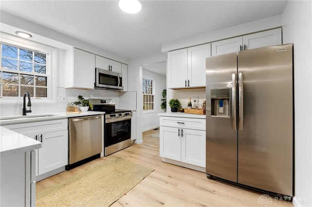 kitchen featuring sink, appliances with stainless steel finishes, tasteful backsplash, light hardwood / wood-style floors, and white cabinets