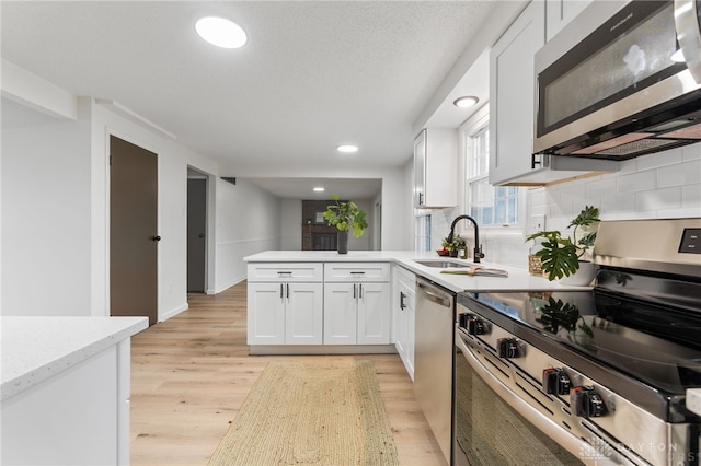 kitchen featuring sink, white cabinets, light hardwood / wood-style floors, kitchen peninsula, and stainless steel appliances