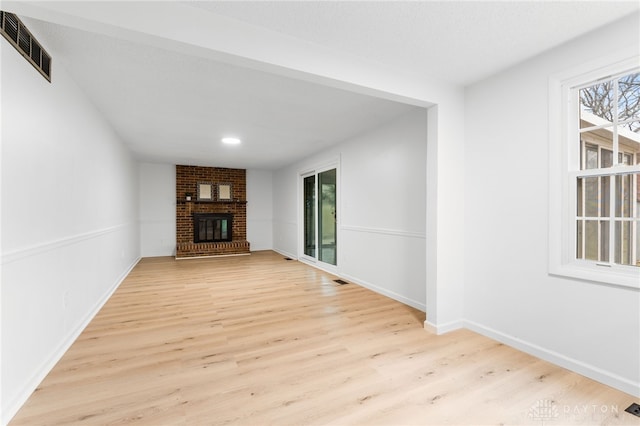 unfurnished living room with a brick fireplace and light hardwood / wood-style flooring