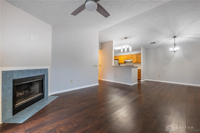 unfurnished living room with dark hardwood / wood-style flooring, ceiling fan with notable chandelier, a tile fireplace, and a textured ceiling