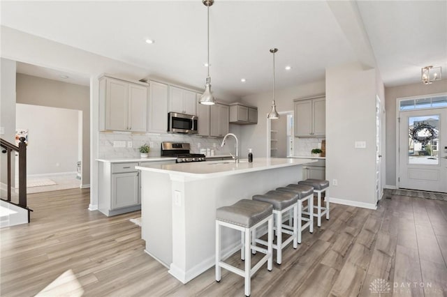 kitchen featuring gray cabinets, sink, light hardwood / wood-style floors, stainless steel appliances, and a center island with sink