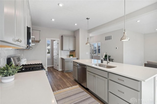 kitchen featuring gray cabinets, decorative light fixtures, sink, stainless steel appliances, and a center island with sink