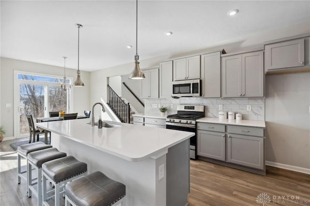 kitchen featuring sink, gray cabinetry, hanging light fixtures, stainless steel appliances, and a kitchen island with sink