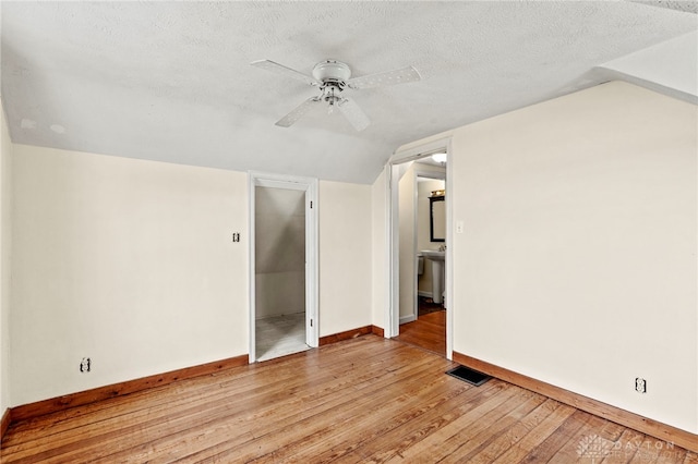 empty room with lofted ceiling, ceiling fan, light hardwood / wood-style flooring, and a textured ceiling