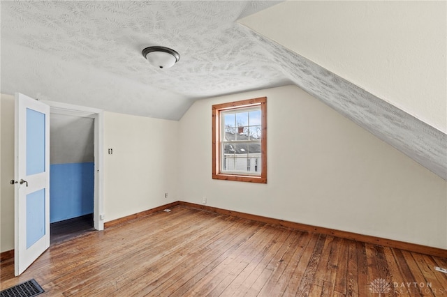 additional living space featuring lofted ceiling, wood-type flooring, and a textured ceiling