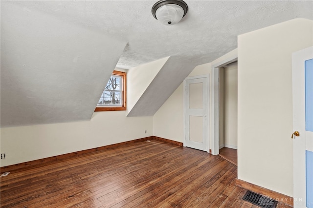 additional living space featuring lofted ceiling, a textured ceiling, and dark hardwood / wood-style flooring