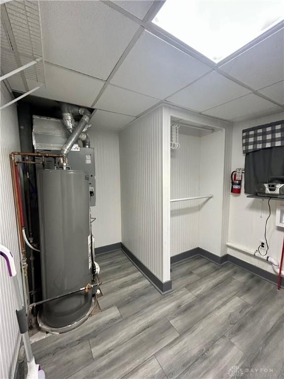 basement with hardwood / wood-style floors, a paneled ceiling, and water heater