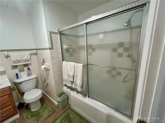 full bathroom featuring vanity, tile walls, bath / shower combo with glass door, and toilet