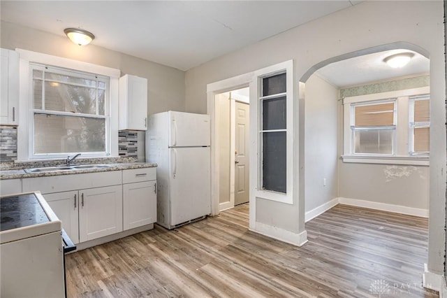 kitchen featuring sink, white cabinetry, stove, white refrigerator, and light hardwood / wood-style floors