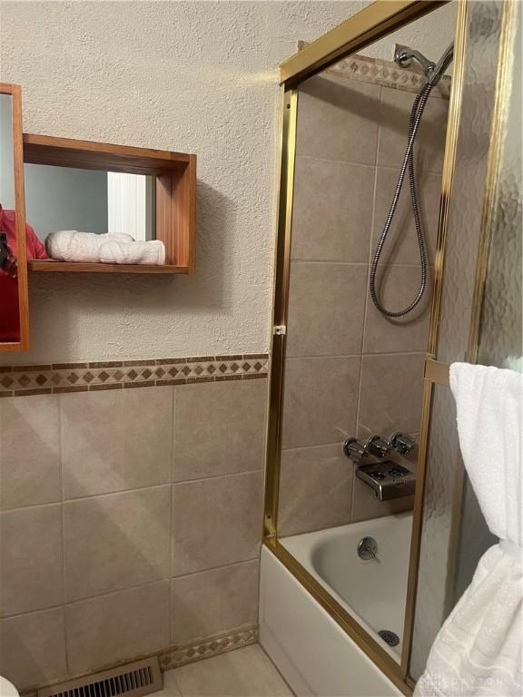 full bathroom with tile patterned flooring, visible vents, bath / shower combo with glass door, and tile walls